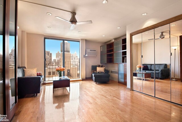 living room with ceiling fan, a wall mounted air conditioner, and light hardwood / wood-style flooring