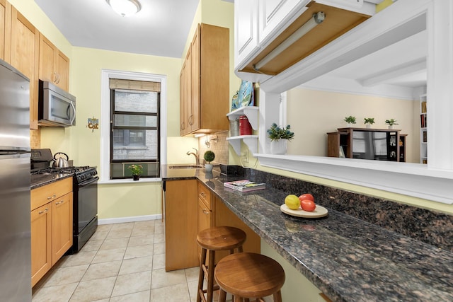 kitchen featuring light tile patterned floors, a breakfast bar, appliances with stainless steel finishes, dark stone counters, and tasteful backsplash