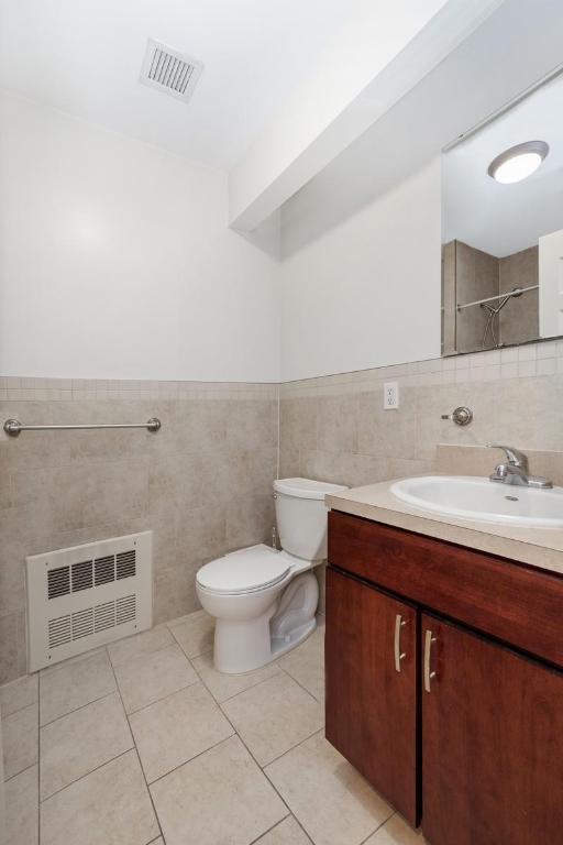 bathroom featuring radiator, tile walls, vanity, tile patterned floors, and toilet