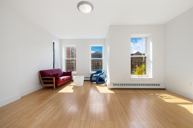 living area with a baseboard heating unit, baseboards, and light wood-style floors