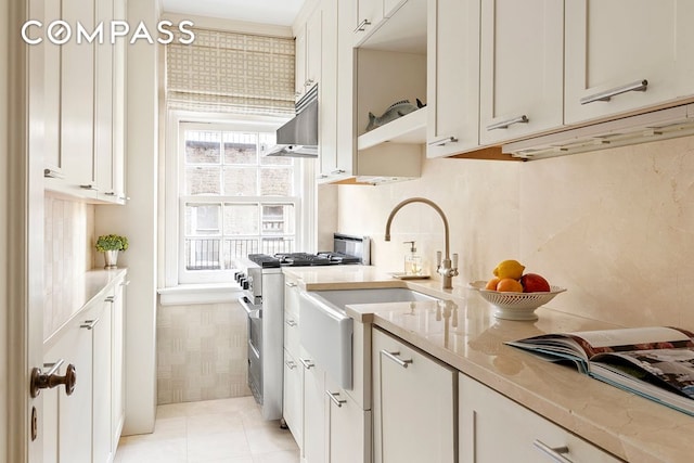 kitchen featuring light stone counters, light tile patterned flooring, high end stove, white cabinetry, and wall chimney range hood