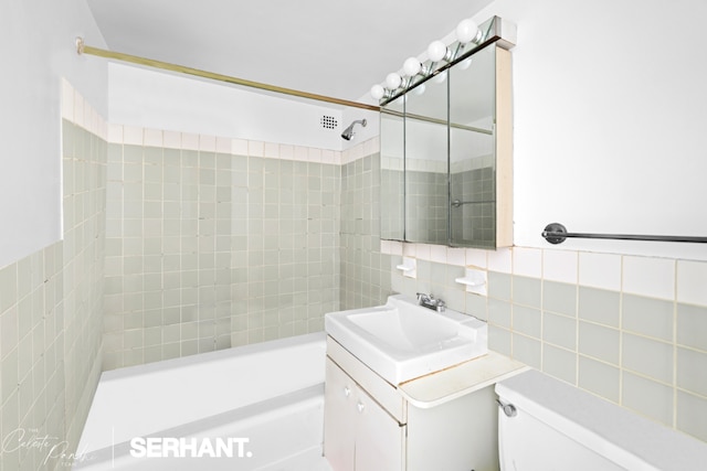 full bathroom with toilet, tasteful backsplash, tile walls, vanity, and tiled shower / bath combo