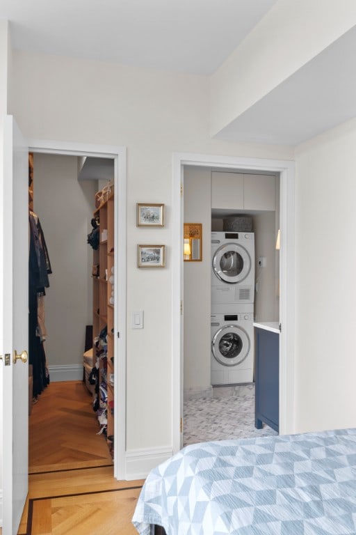 bedroom with a closet, a walk in closet, stacked washer / dryer, and light parquet floors