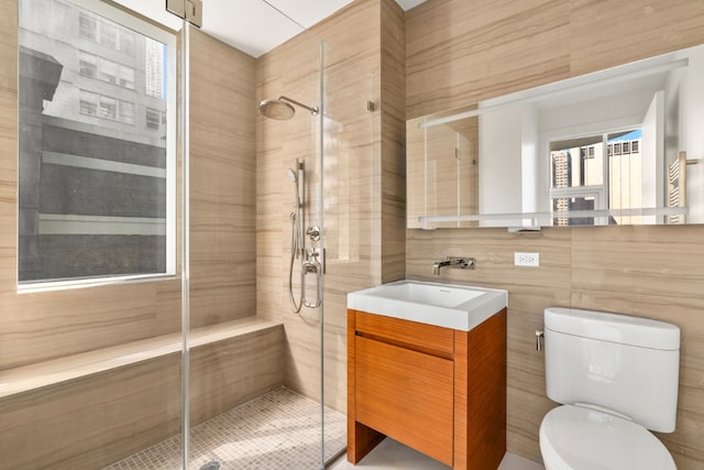 bathroom with vanity, tiled shower, tile walls, and toilet