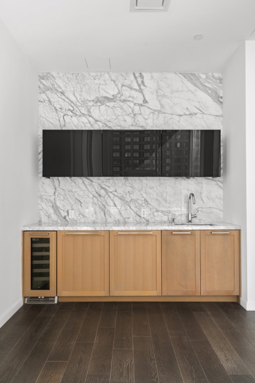 bar featuring dark wood-type flooring, beverage cooler, sink, and light brown cabinets