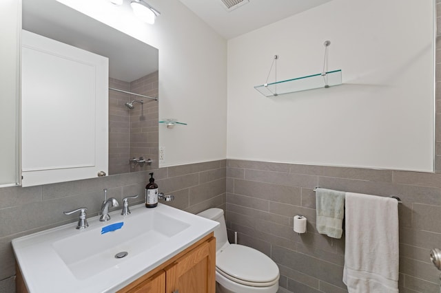 bathroom with toilet, a shower, tile walls, and vanity