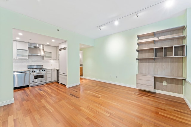 kitchen featuring decorative backsplash, premium appliances, wall chimney exhaust hood, light wood-style flooring, and light countertops