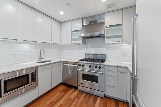 kitchen featuring visible vents, appliances with stainless steel finishes, wood finished floors, a sink, and exhaust hood