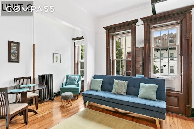 living area with arched walkways, light wood finished floors, radiator, and ornamental molding