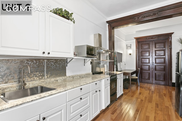 kitchen with black appliances, light wood-style flooring, ornamental molding, backsplash, and wall chimney exhaust hood