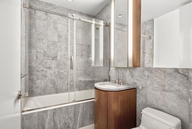 full bathroom with combined bath / shower with glass door, vanity, tile walls, and toilet