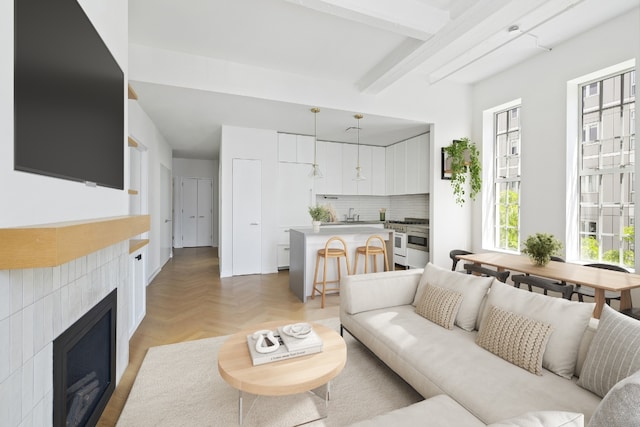 living room with beamed ceiling, a tiled fireplace, and light parquet floors