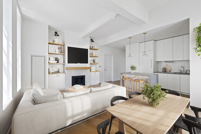 living room with a tiled fireplace, sink, wood-type flooring, and beamed ceiling