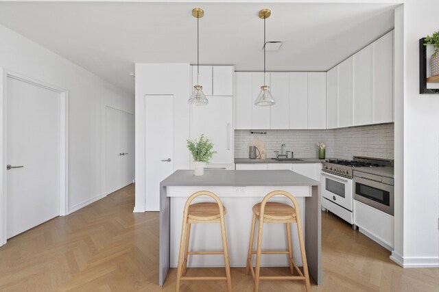 kitchen with a kitchen island, white cabinetry, decorative backsplash, high end stainless steel range oven, and light parquet flooring