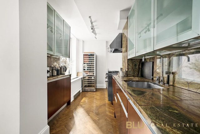 kitchen featuring rail lighting, decorative backsplash, glass insert cabinets, stainless steel range with gas stovetop, and dark stone counters