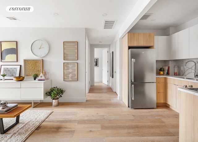 kitchen featuring light wood finished floors, visible vents, a sink, and freestanding refrigerator