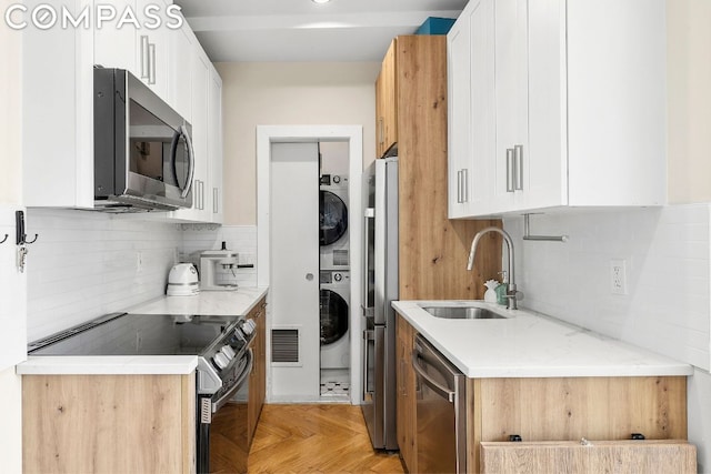 kitchen with stacked washer and dryer, sink, appliances with stainless steel finishes, light parquet flooring, and white cabinets