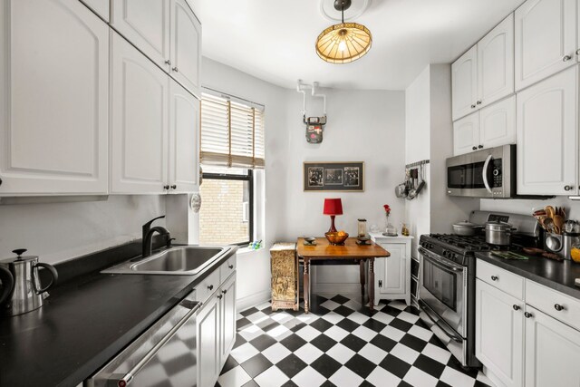 kitchen with stainless steel appliances, a sink, dark floors, dark countertops, and white cabinetry