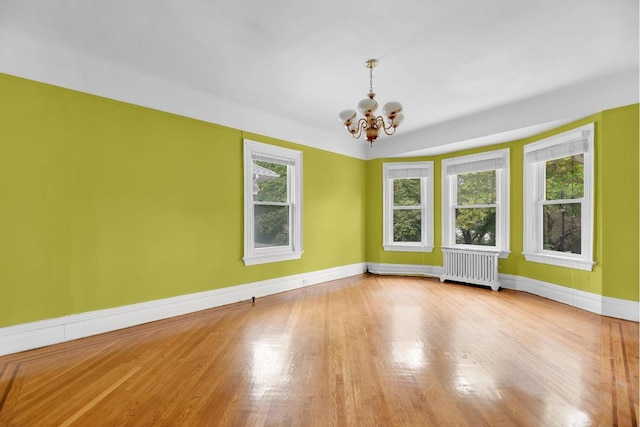 unfurnished room with baseboards, an inviting chandelier, wood finished floors, and radiator heating unit