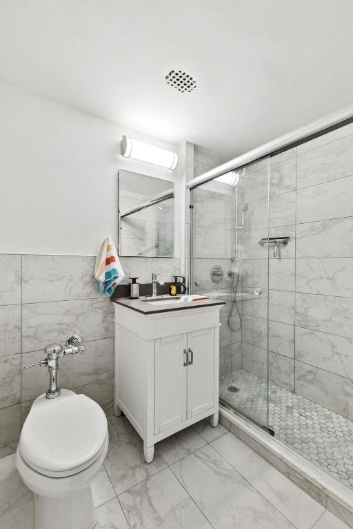 bathroom featuring vanity, toilet, tile walls, and a shower with shower door