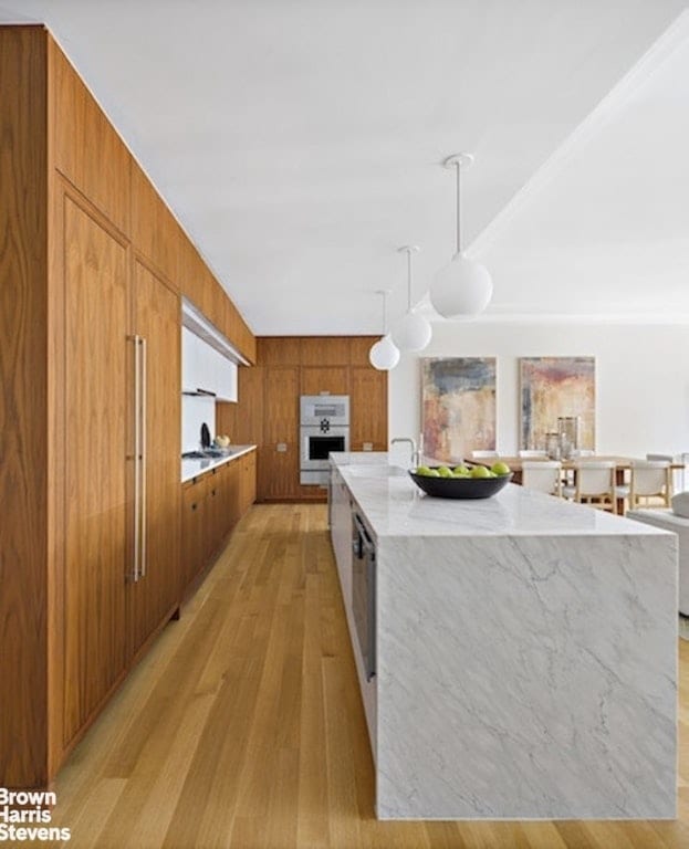 kitchen featuring light hardwood / wood-style floors, wooden walls, a large island, pendant lighting, and light stone counters