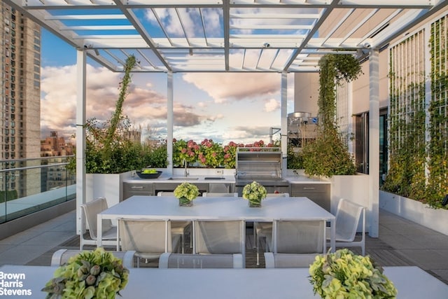 patio terrace at dusk with sink, an outdoor kitchen, and a pergola