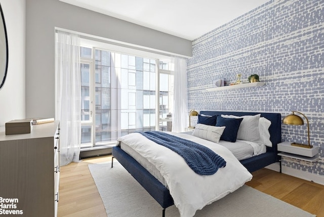 bedroom with light wood-style flooring, an accent wall, and wallpapered walls