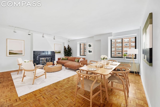 dining area with light parquet floors, rail lighting, and a fireplace