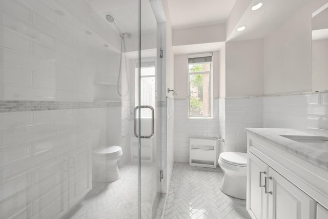 bathroom featuring tile walls, vanity, a shower with shower door, and toilet