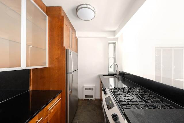 kitchen with brown cabinetry, stone finish floor, a sink, and appliances with stainless steel finishes
