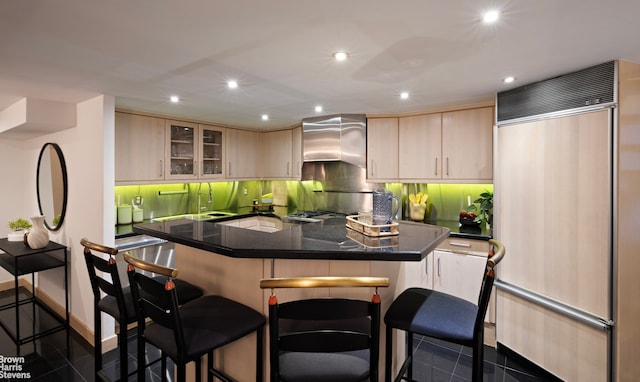 kitchen with light brown cabinets, paneled fridge, glass insert cabinets, and a breakfast bar area