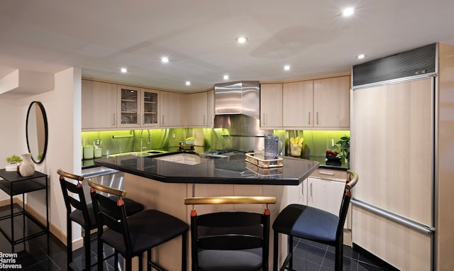 253 W 73rd St Unit 2G, New York City, NY 10023 - kitchen featuring paneled built in refrigerator, light brown cabinets, a kitchen breakfast bar, wall chimney exhaust hood, and recessed lighting