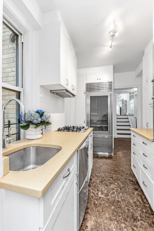 kitchen with appliances with stainless steel finishes, white cabinetry, tasteful backsplash, and sink