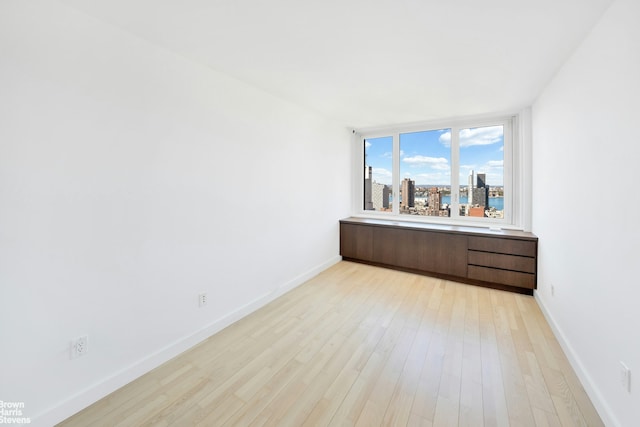 unfurnished room featuring baseboards, light wood-type flooring, and a city view