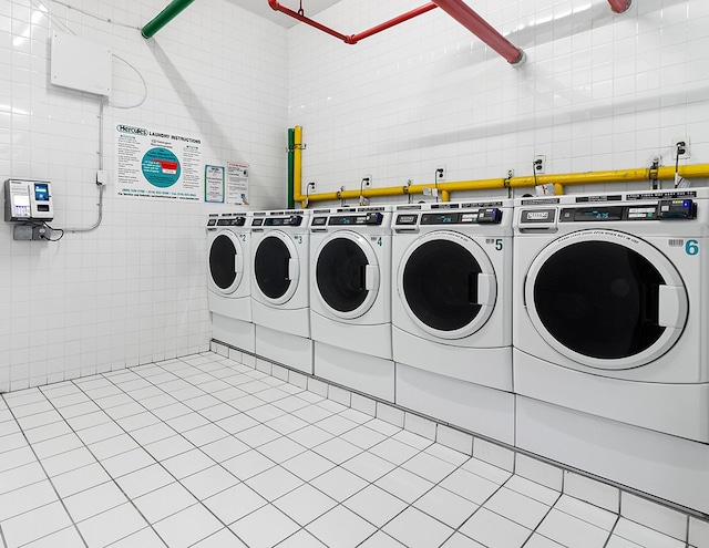 common laundry area with light tile patterned floors, washer and clothes dryer, and tile walls