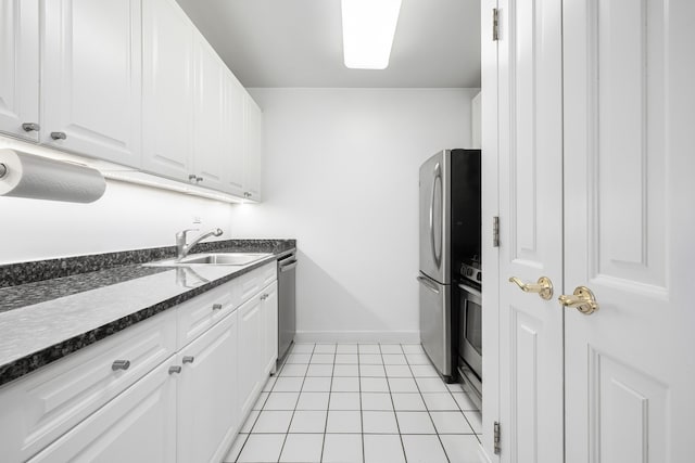 kitchen with light tile patterned floors, appliances with stainless steel finishes, white cabinetry, a sink, and baseboards