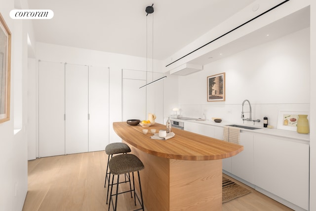 kitchen featuring white cabinets, a breakfast bar, a center island, light wood-style floors, and a sink