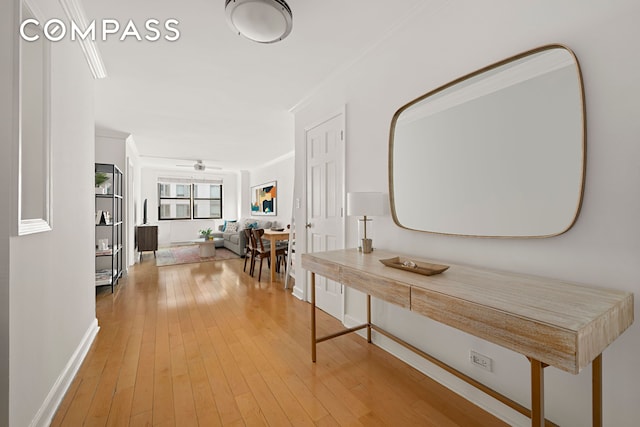 corridor with light wood-style flooring, ornamental molding, and baseboards