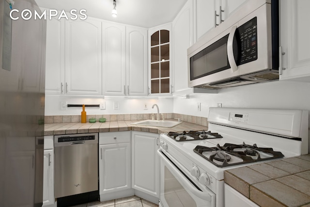 kitchen featuring glass insert cabinets, tile counters, white appliances, white cabinetry, and a sink