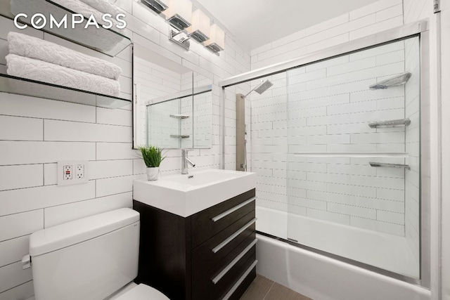 full bathroom featuring tile walls, bath / shower combo with glass door, vanity, and toilet