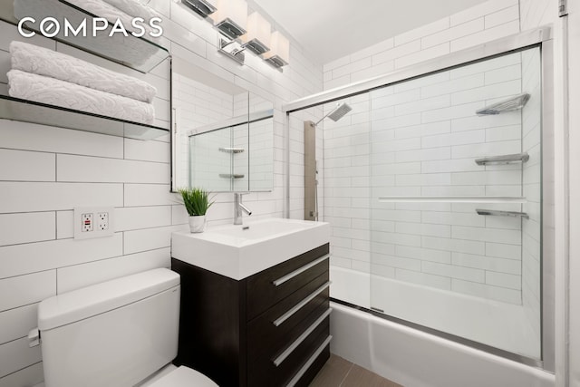 bathroom featuring tile walls, toilet, vanity, and shower / bath combination with glass door