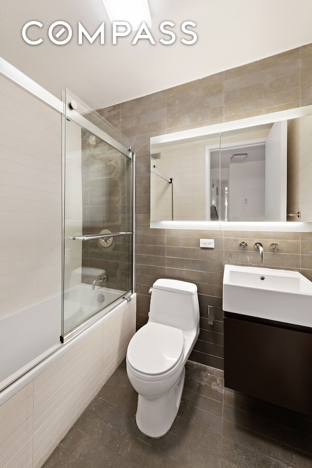 full bath with tile patterned floors, tiled shower / bath, toilet, tile walls, and vanity