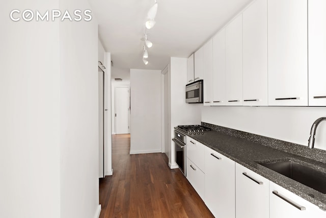 kitchen with dark stone countertops, a sink, dark wood-type flooring, appliances with stainless steel finishes, and white cabinetry