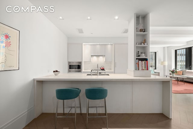 kitchen featuring light countertops, stainless steel microwave, white cabinetry, a sink, and modern cabinets