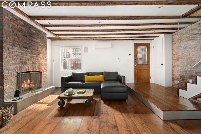 living room featuring a wall mounted air conditioner, beamed ceiling, hardwood / wood-style floors, and a brick fireplace