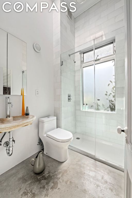 bathroom with toilet, concrete flooring, a shower with shower door, and sink