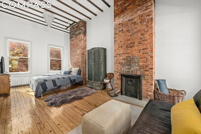 bedroom with a high ceiling, beamed ceiling, a fireplace, and light hardwood / wood-style flooring