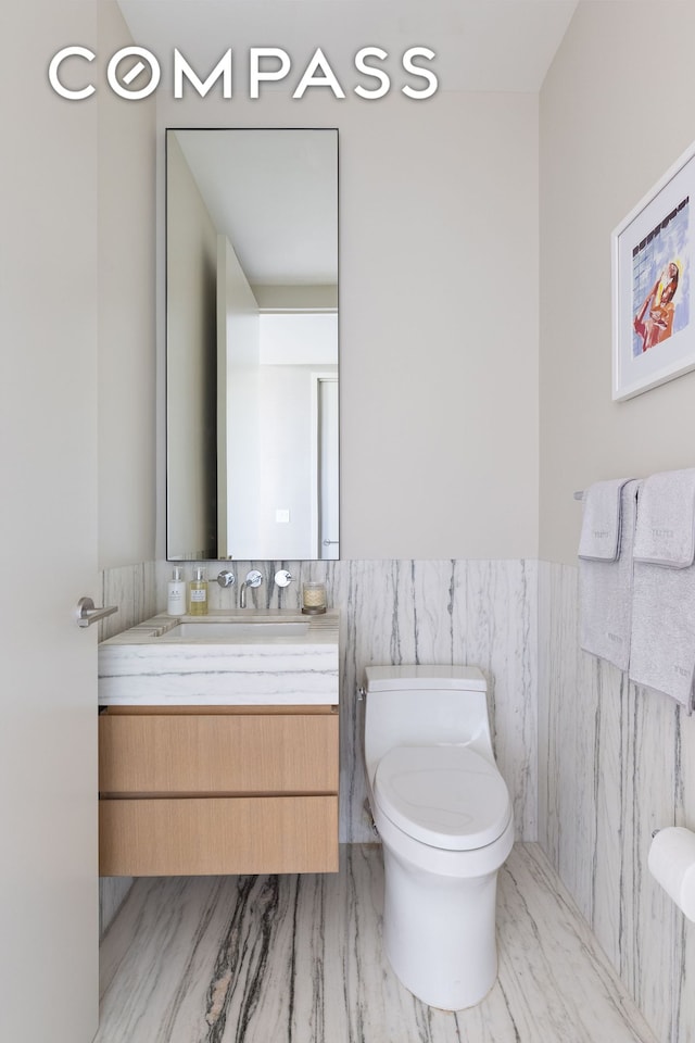 half bath with a wainscoted wall, toilet, vanity, and tile walls