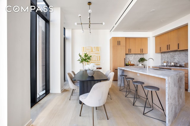 kitchen featuring light wood-type flooring, a sink, backsplash, stainless steel gas stovetop, and a breakfast bar area