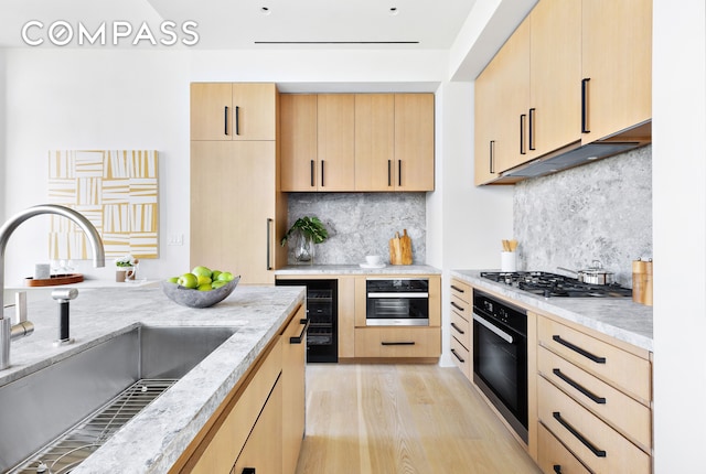 kitchen with a sink, black oven, and light brown cabinetry